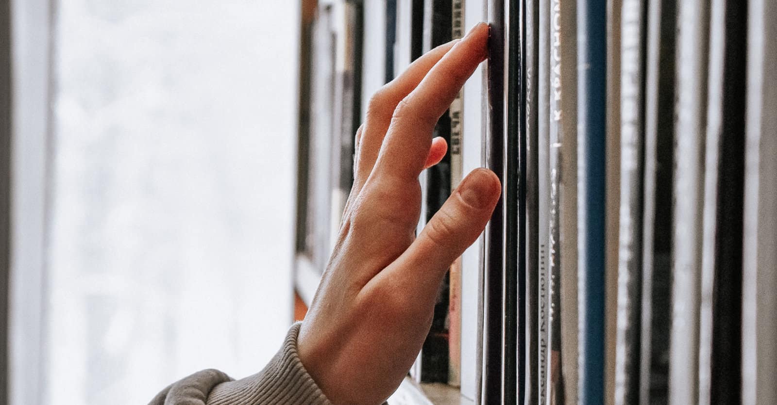 Hand touching books on a shelf, perhaps in a library (Credit: Guzel Maksutova, Unsplash)